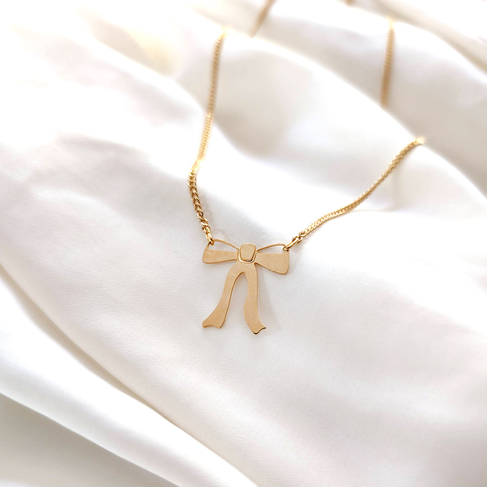 Gold necklace with a ribbon bow pendant hangs from both sides on a white background 