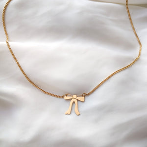 Gold necklace with a ribbon bow pendant hangs from both sides on a white background 