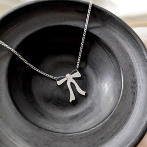 Silver necklace with a ribbon bow pendant hangs from both sides on a black round dish