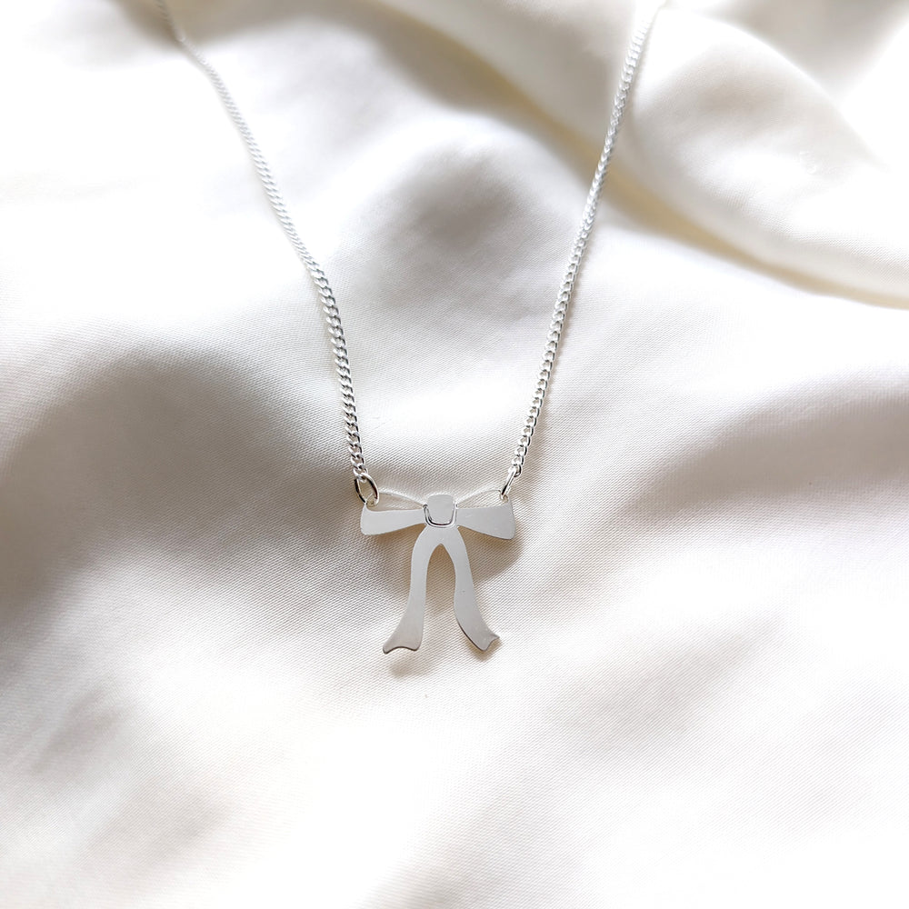 Silver necklace with a ribbon bow pendant hangs from both sides on a white background 